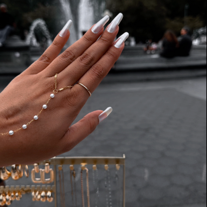 Hand with white nail polish and gold jewelry against a blurred fountain background