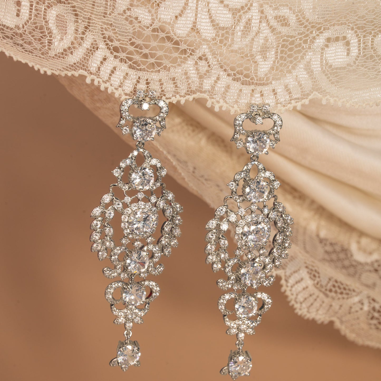 Pair of ornate diamond earrings on a lace fabric background