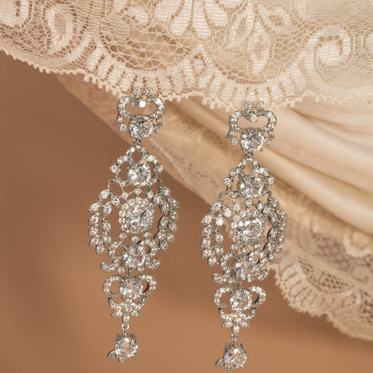 Pair of ornate diamond earrings on a lace fabric background