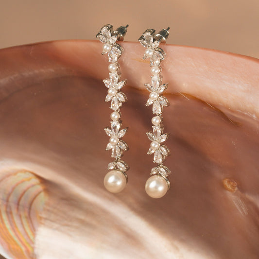Pearl and crystal drop earrings on a shell with a blurred background