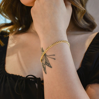 Close-up of a person's wrist wearing a gold bracelet with a butterfly tattoo on a blurred background